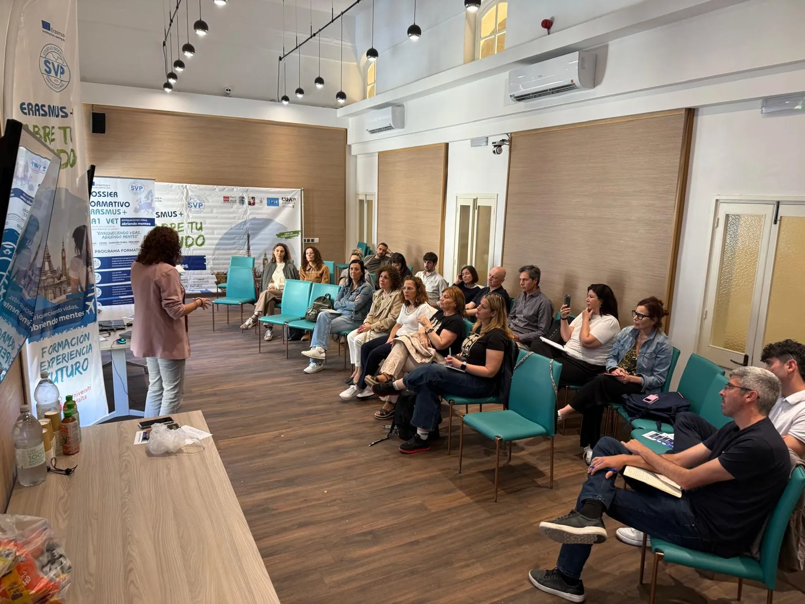 A speaker addressing a group of teachers seated in a semicircle