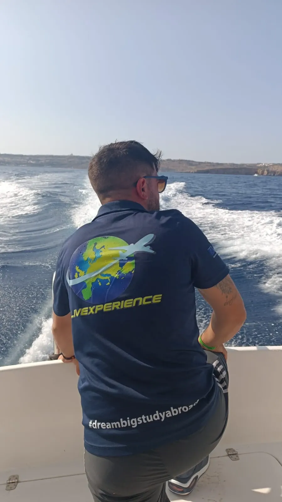 A LIVEXPERIENCE team member on a boat, seen from behind, wearing a shirt with the logo
