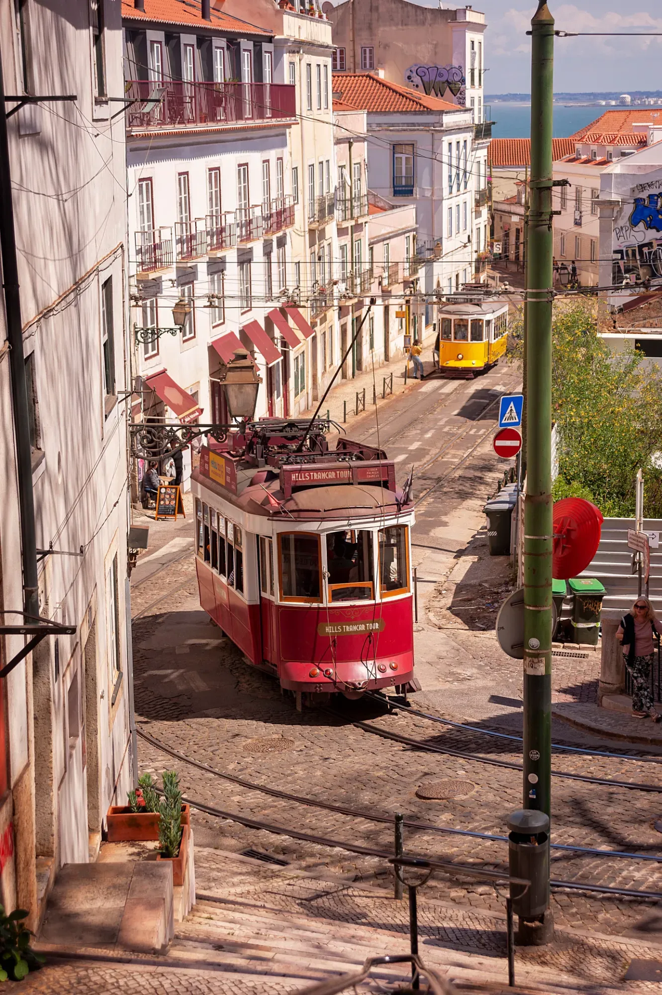 Trams on a cobbled street in Lisbon, with the river Tagus in the background
